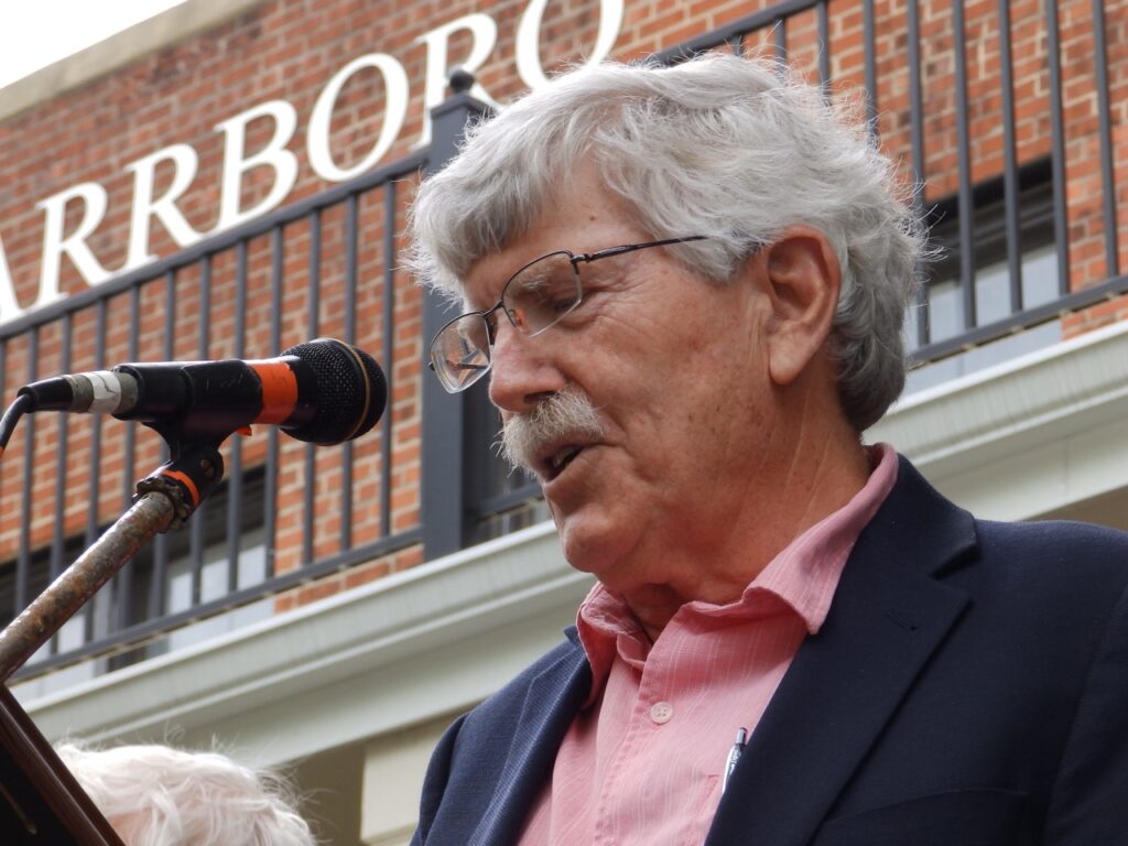Close-up of Jay Bryan reading at microphone in front of building